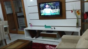Un salon avec un téléviseur à écran plat fixé à un mur blanc, un meuble de rangement blanc, un canapé beige et un tapis rouge.