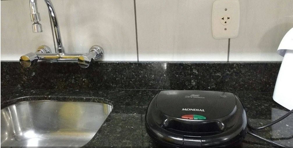 Una cocina con encimera de granito, pileta de acero inoxidable y una tetera eléctrica negra con la etiqueta 'MONDIAL'.
