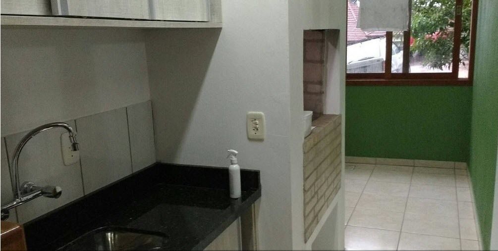 Uma cozinha compacta com bancada preta, pia de aço inoxidável e torneira branca. Há uma janela com vista para o exterior.