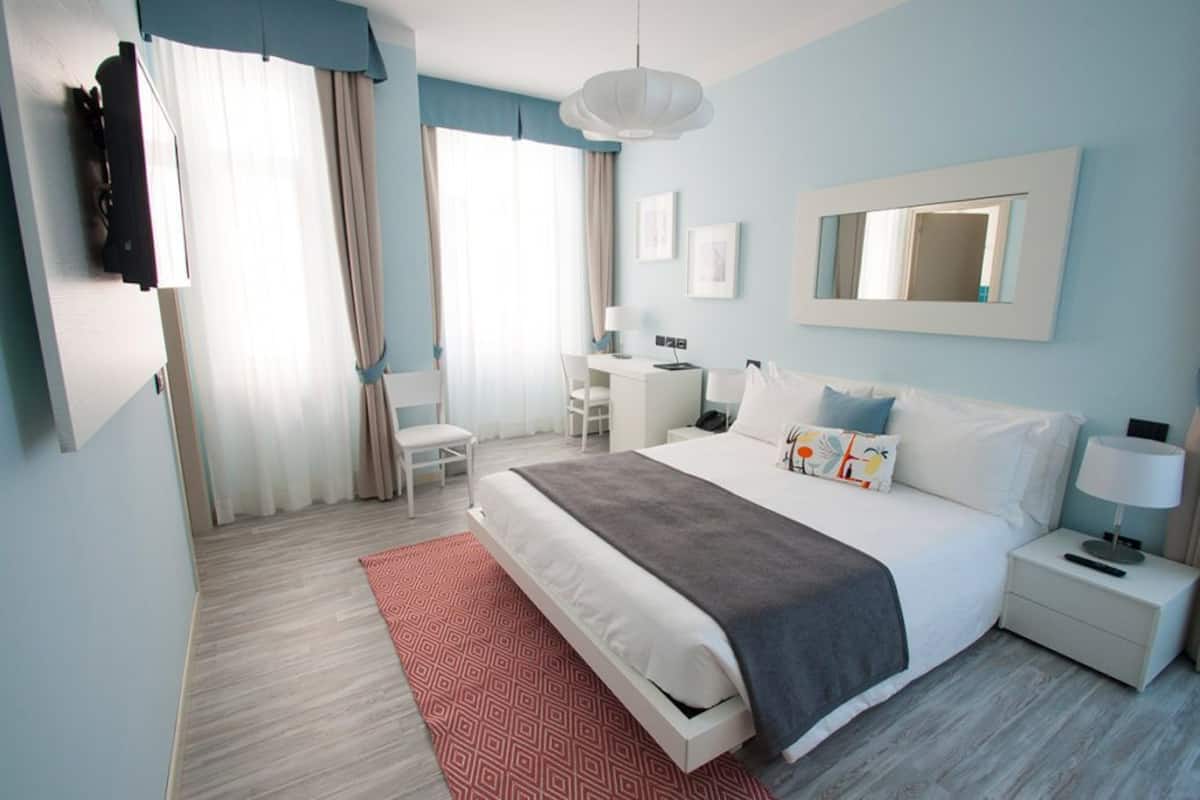 A modern hotel room with a large bed, a desk, a chair, and a TV.