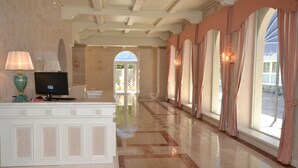 A hotel lobby with a reception desk, a television, and a large arched window with curtains. - Hotel Villa Bernt (Grado)
