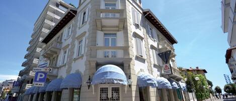 Un hotel de varios pisos llamado "Villa Bernt" con un estilo arquitectónico clásico, que presenta una entrada destacada con toldo, múltiples balcones y un letrero de estacionamiento que indica una zona de estacionamiento de 30 minutos.