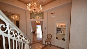 A grand hallway with a white ornate railing, a chandelier, and a display of framed pictures on the wall. - Hotel Villa Bernt (Grado)