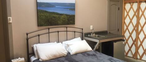 A bedroom with a bed, a small table, and a painting of a landscape.