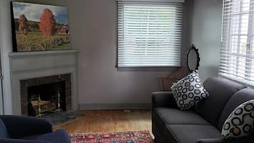 Una sala de estar con chimenea, un sofá, una alfombra estampada y un cuadro en la pared.