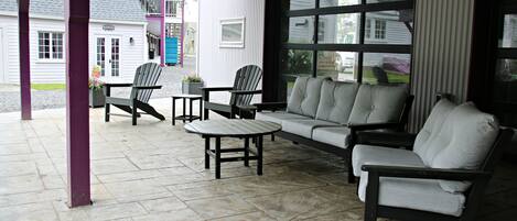 Un espacio cubierto con patio, un sofá, dos sillas Adirondack y una mesita.