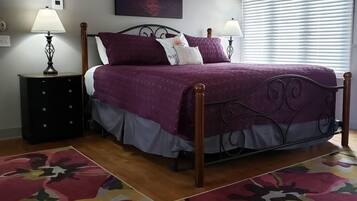 A bedroom with a bed, two nightstands, a painting, and a window with blinds.