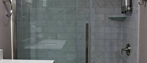 A modern bathroom with a glass-enclosed shower, a white marble sink, and a tiled floor.