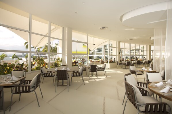 Un amplio comedor interior con grandes ventanales, mobiliario moderno y vistas a la ciudad.