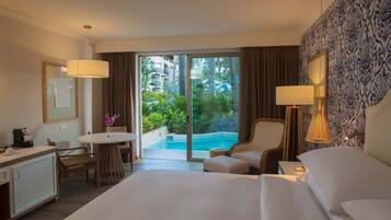 Habitación de hotel con una cama grande, un escritorio con una silla, una mesita con una silla, un sofá y vistas a una piscina y vegetación.