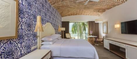 Hotelkamer met een groot bed, een plafondventilator, een televisie en uitzicht op palmbomen.