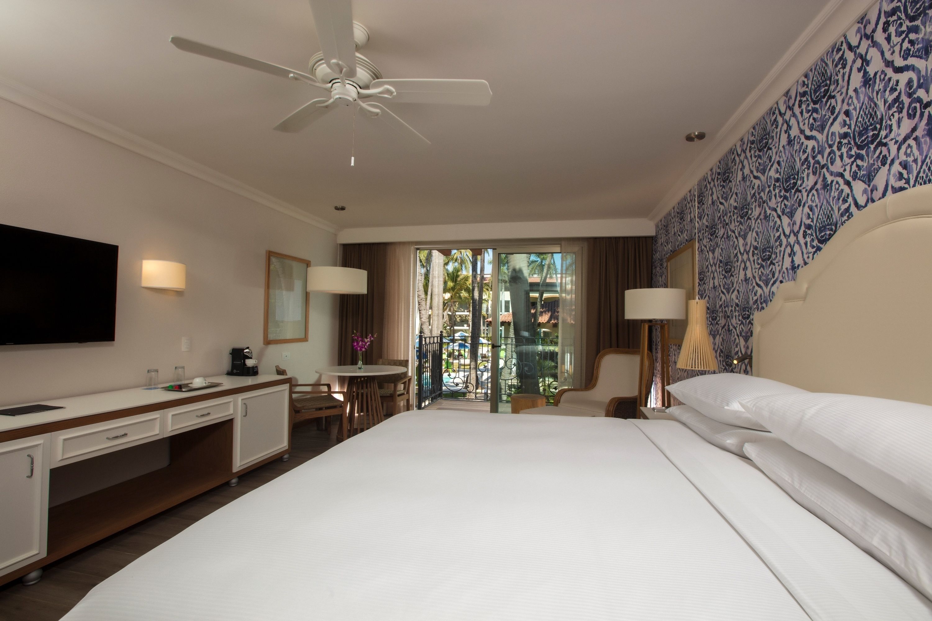 Habitación de hotel con cama, escritorio, silla y balcón con vistas.