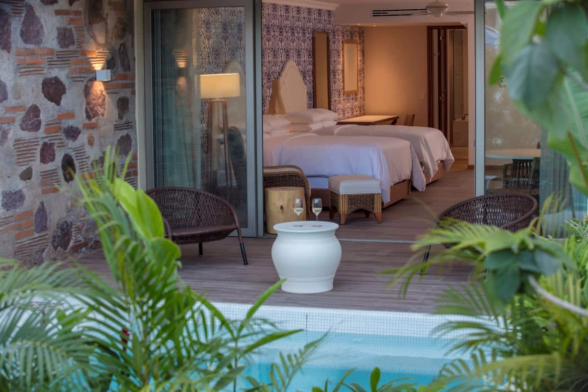 Une chambre d’hôtel avec un grand lit, un coin salon avec une table et des chaises, une petite table avec un vase et une vue sur la piscine.