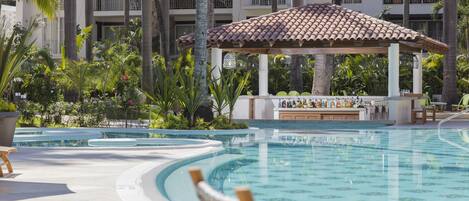 Área de piscina en un resort con un pabellón, palmeras y un bar.