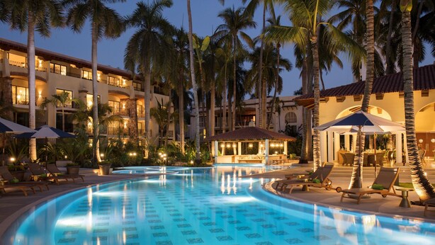A swimming pool with lounge chairs and umbrellas, surrounded by palm trees and hotel buildings. - The Hacienda at Krystal Grand Puerto Vallarta (Puerto Vallarta)