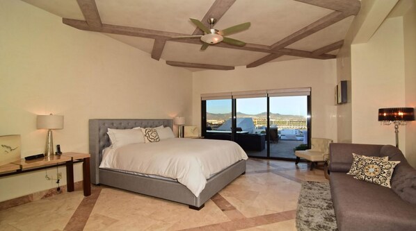 A bedroom with a large bed, a ceiling fan, a sofa, and a view of a cityscape through a sliding door.