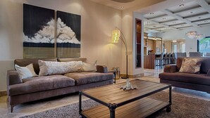 A spacious living room with a brown leather sofa, a wooden coffee table, and a large painting of clouds on the wall. - Villa Vegas by Cabo Platinum (Cabo San Lucas)