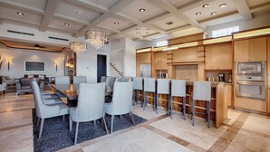 A spacious living area with a high ceiling, a dining area with grey upholstered chairs, and a kitchen with wooden cabinets and stainless steel appliances. - Villa Vegas by Cabo Platinum (Cabo San Lucas)