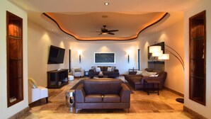 A spacious living room with a large brown sofa, a smaller armchair, a coffee table, and a TV mounted on the wall. - Villa Vegas by Cabo Platinum (Cabo San Lucas)