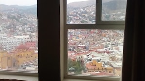 A cityscape through a window with multiple panes, featuring a variety of buildings and a mountainous backdrop.