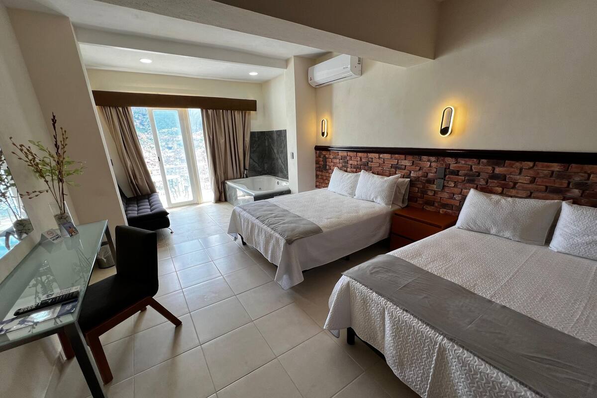 A hotel room with two beds, a glass table, a desk, and a view of the city.
