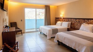 A hotel room with two beds, a desk, a chair, and a balcony with a view of the mountains.