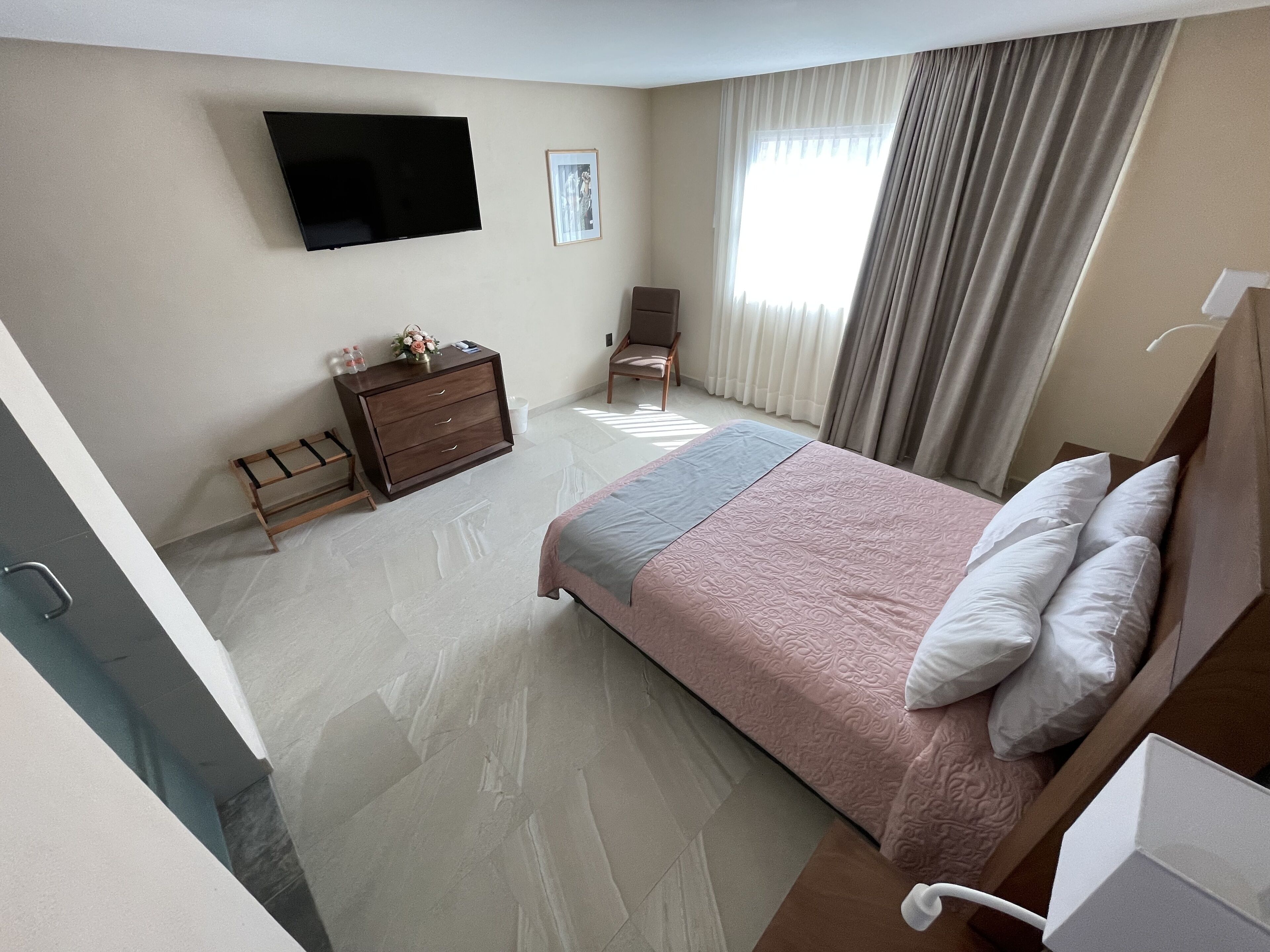 Quarto de hotel com cama, televisão na parede, cômoda de madeira e uma cadeira.