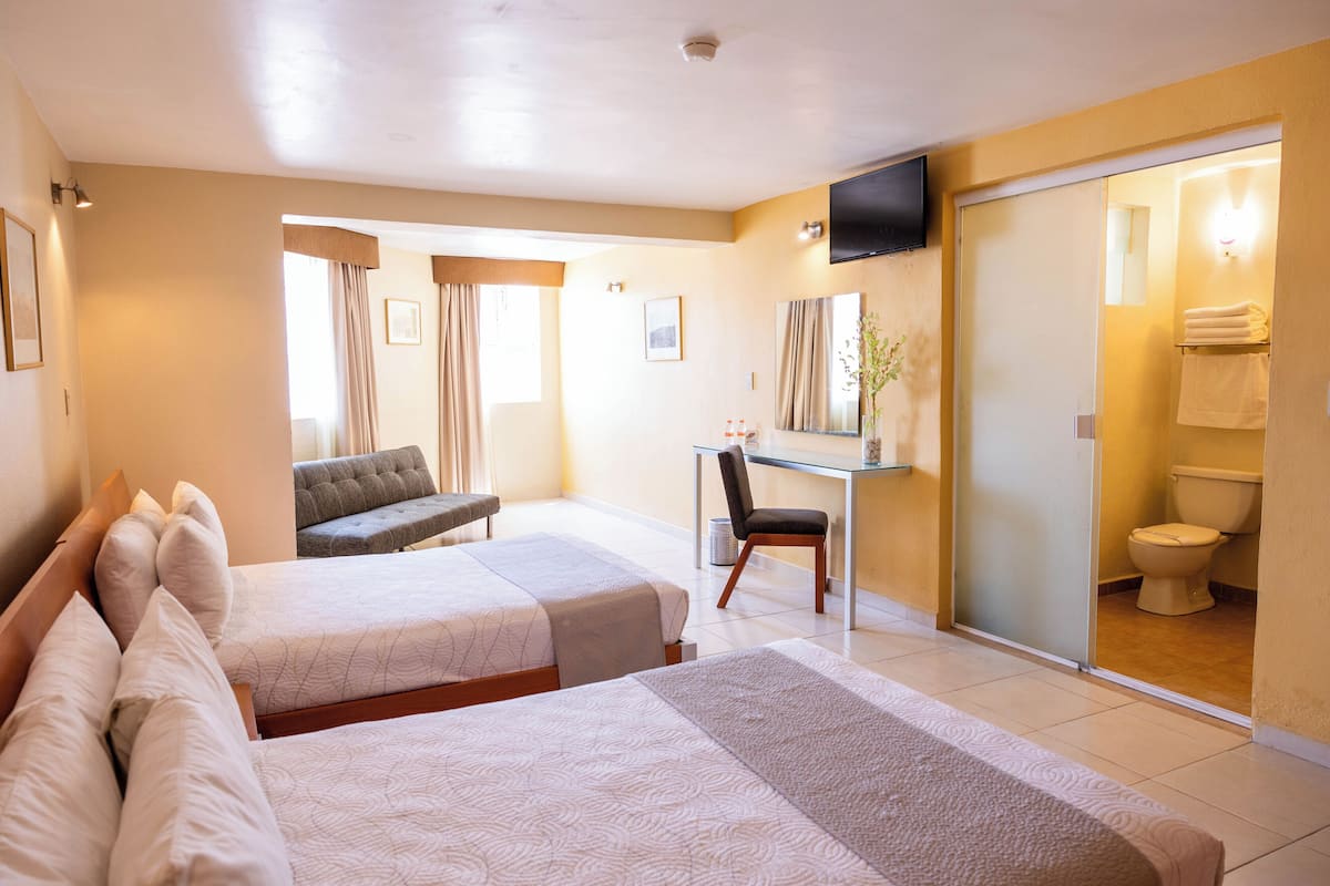 A hotel room with two beds, a desk, a chair, a TV, and a bathroom with a toilet and sink.