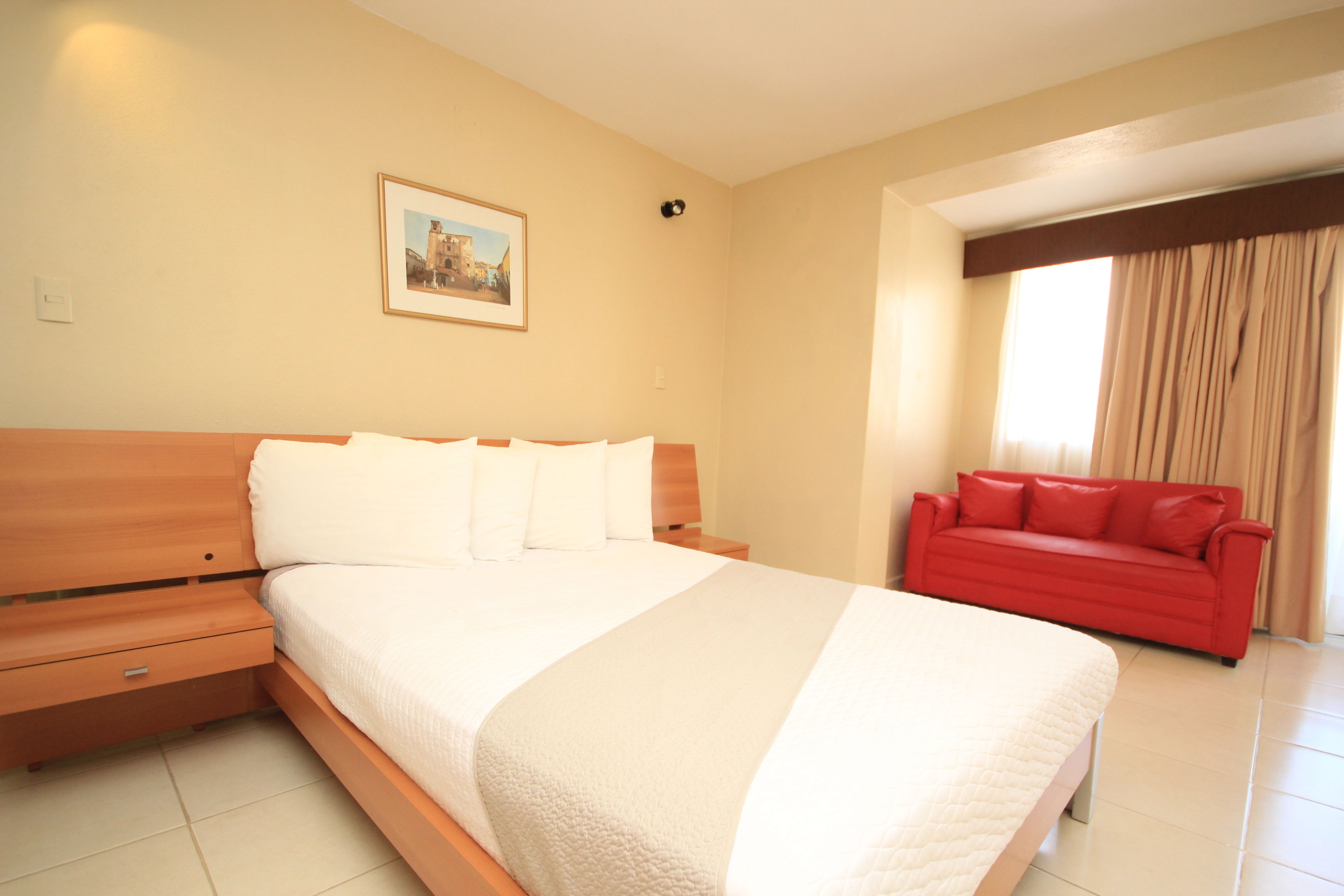 Ein Hotelzimmer mit einem großen Bett, einem roten Sofa und einem gerahmten Bild an der Wand.