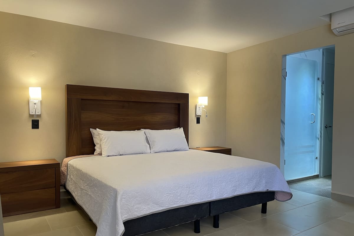 A neatly made bed with a wooden headboard, two bedside tables, and wall-mounted lights.