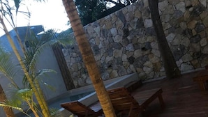 Een houten terras met lounge stoelen, palmbomen en een stenen muur.