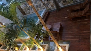Een moderne binnentuin met een stenen muur, houten vloer en een palmboomplanter met verlichting.