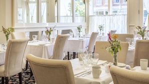 A well-lit dining area with tables set for service, large windows with curtains, and a view of buildings outside. - Belfast Bay Inn (Belfast)