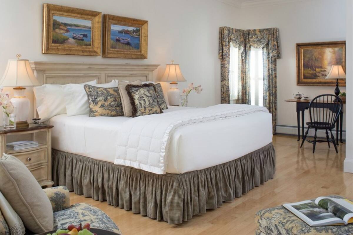 A neatly arranged bedroom with a large bed, two bedside tables with lamps, a chair, and two framed pictures on the wall.