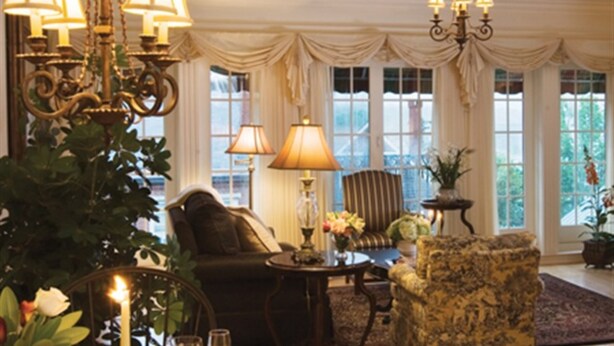 A well-lit room with a chandelier, a large window with curtains, a sofa, a chair, and a table with a vase of flowers. - Belfast Bay Inn (Belfast)