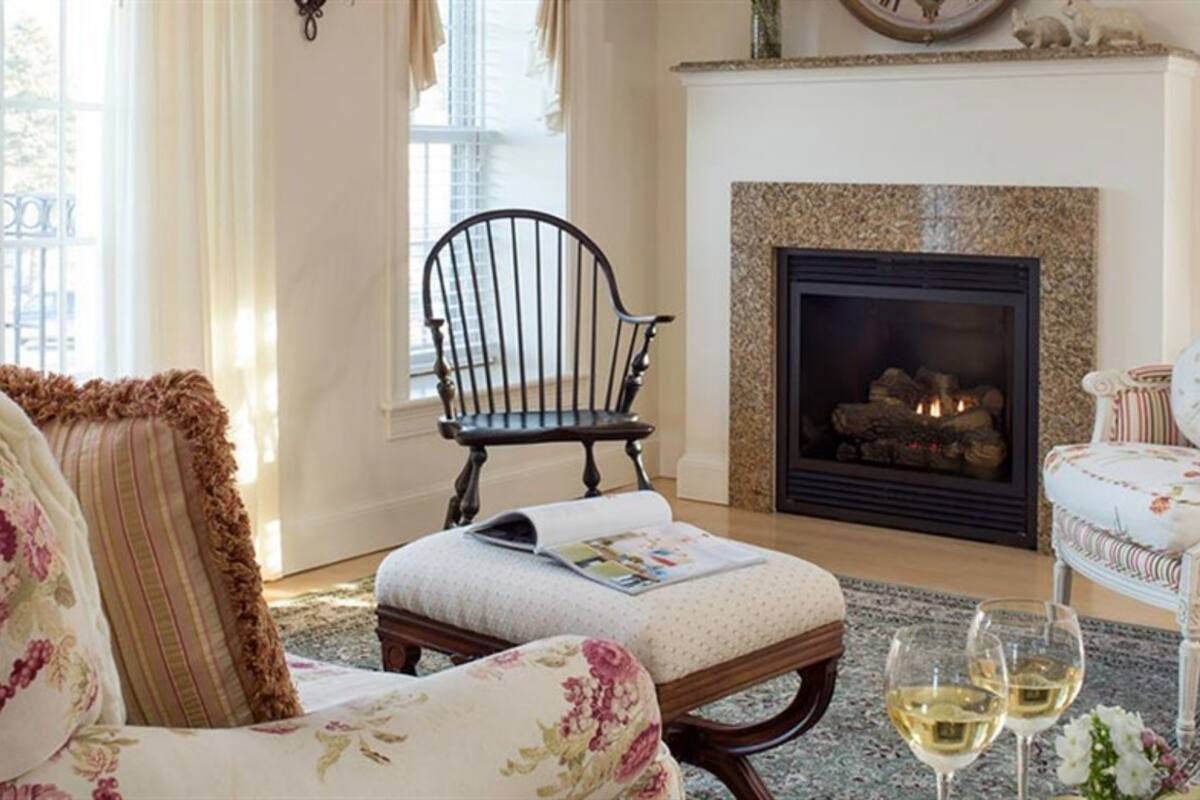 A cozy living room with a fireplace, a wooden bench, and two chairs.
