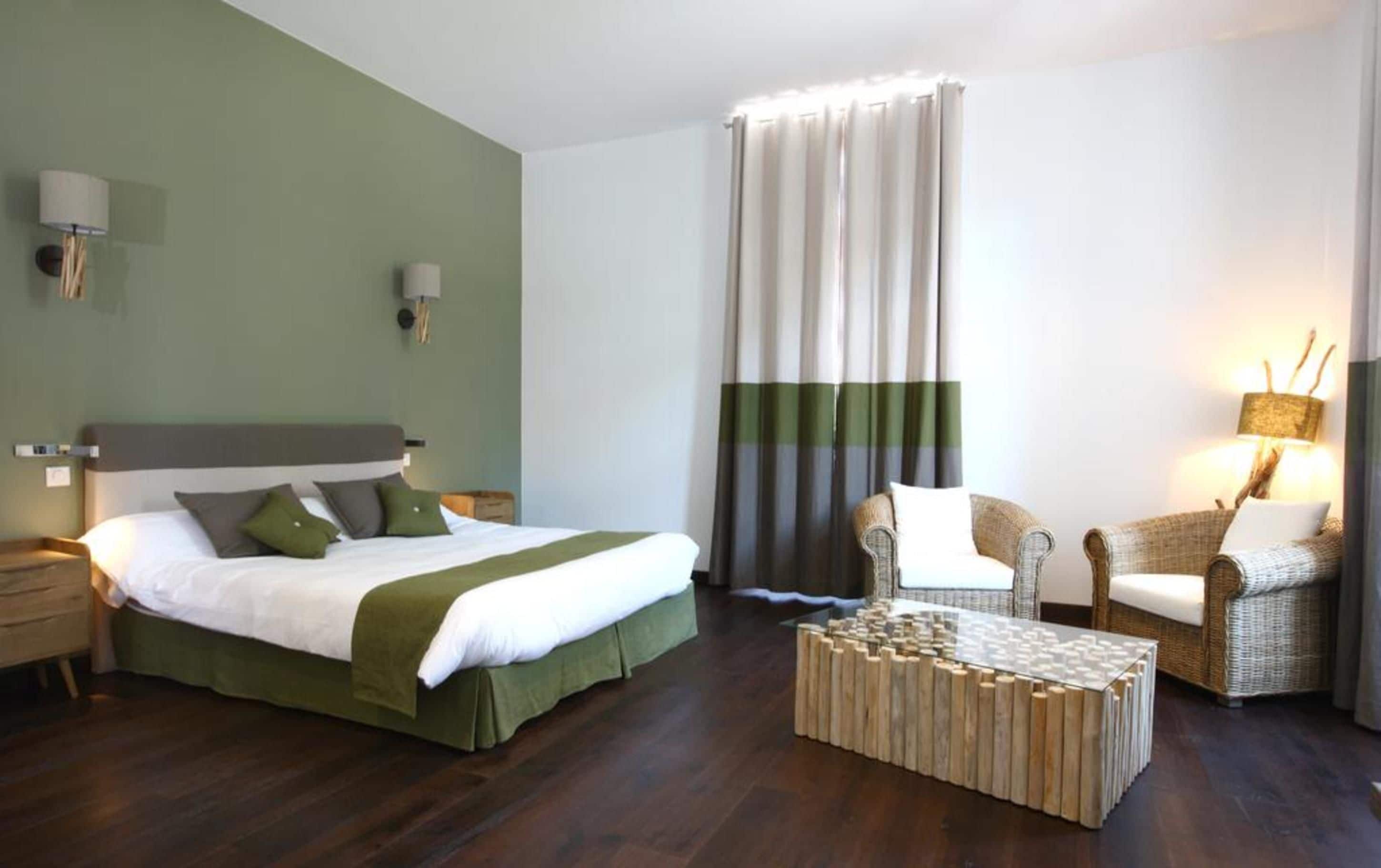 Ein Hotelzimmer mit Bett, Sessel, Couchtisch und Vorhang.