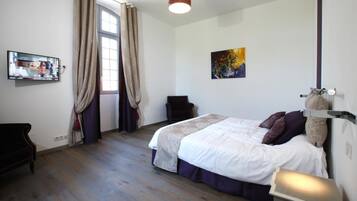 A bedroom with a bed, a chair, a painting, and a television on the wall.