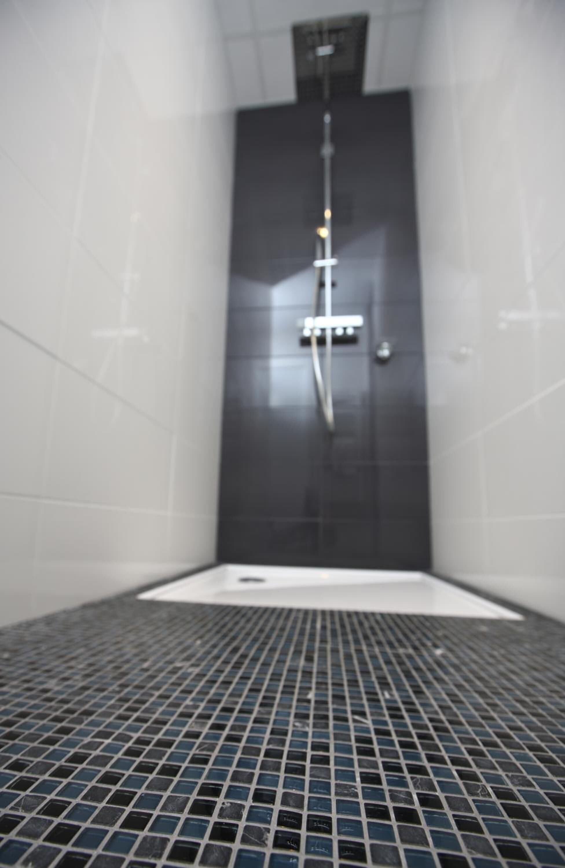 Een badkamer met betegelde vloer, douche en wit wastafel.
