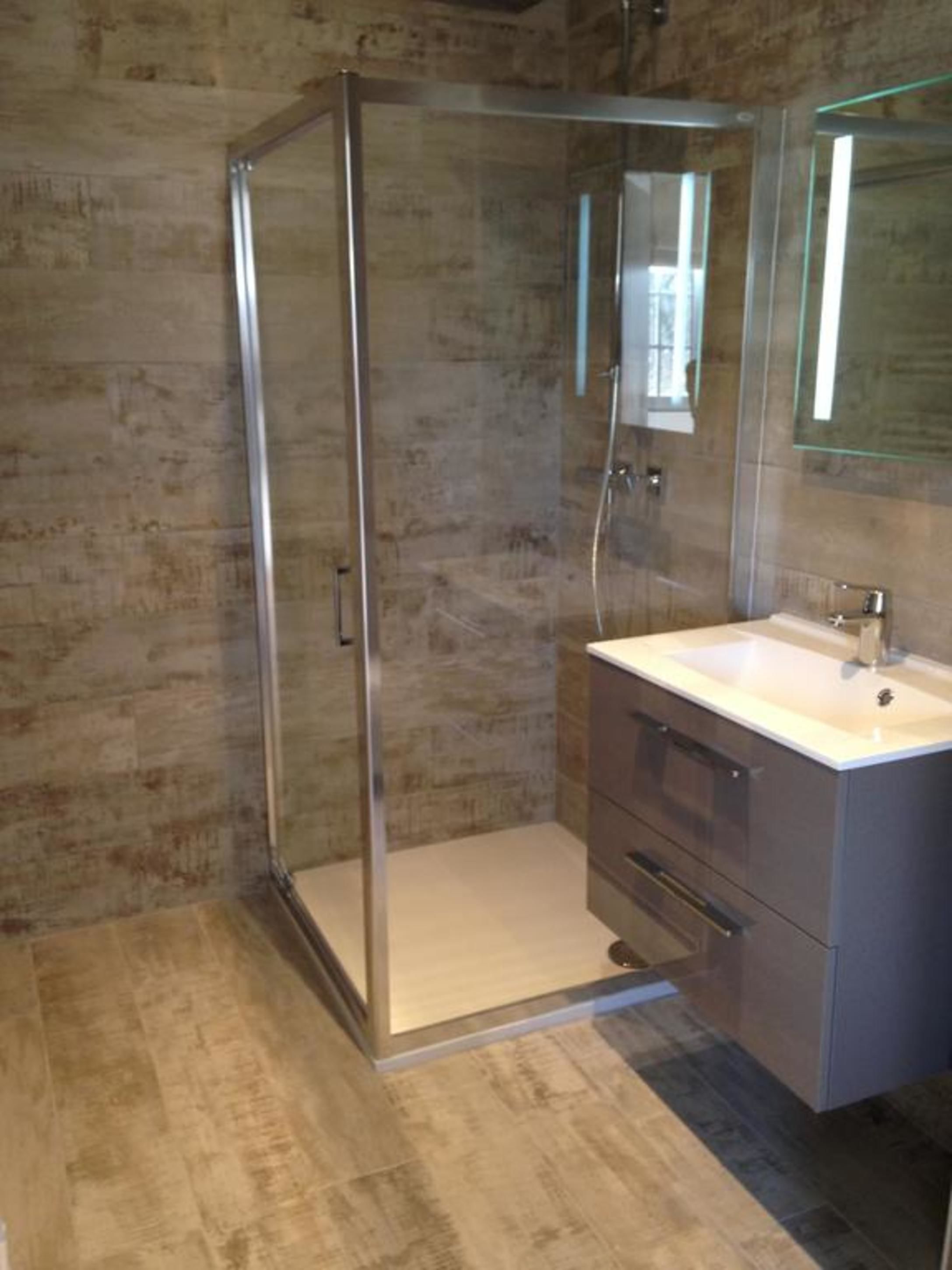 Un baño moderno con cabina de ducha de vidrio, un lavabo blanco y un espejo grande.
