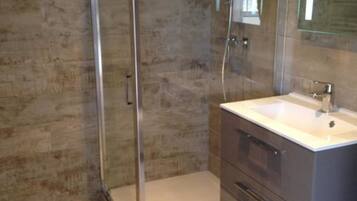 Un baño moderno con cabina de ducha de vidrio, un lavabo blanco y un espejo grande.
