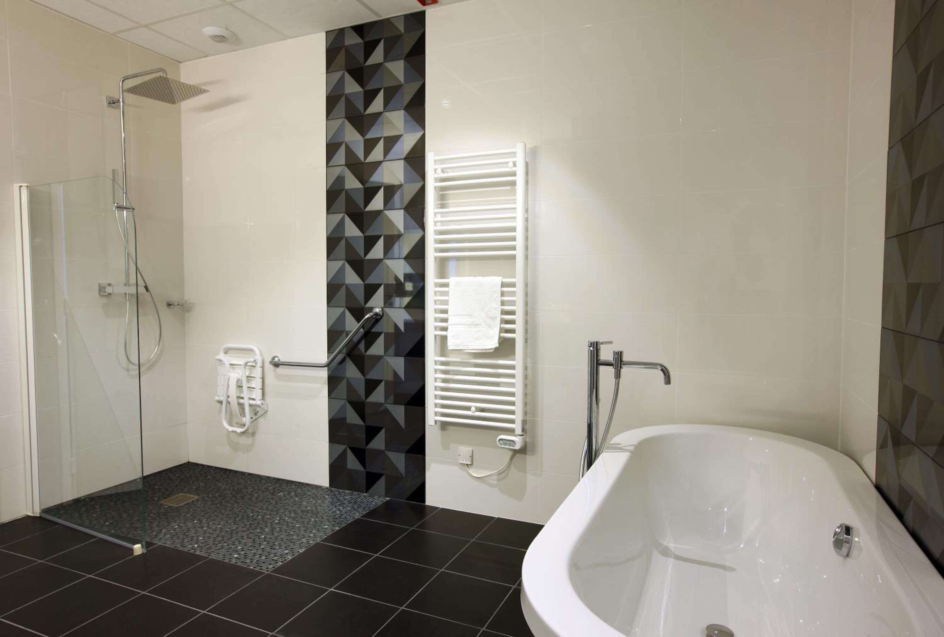 Un baño moderno con ducha de vidrio, una bañera independiente y un perchero para toallas.