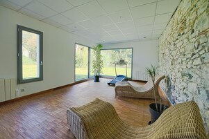 Una habitación amplia con ventanas grandes, pared de piedra y muebles de mimbre.