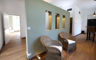 Un interior moderno con sillas de mimbre, suelo de madera e iluminación empotrada en una pared.