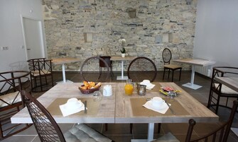 Un comedor con pared de piedra, una mesa de madera dispuesta para el desayuno y sillas de mimbre.