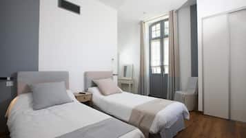 Una habitación de hotel con dos camas individuales, un escritorio, una silla, un armario y una ventana con cortinas.