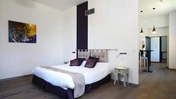 A modern bedroom with a large bed, a small bedside table, a chair, and a painting on the wall.