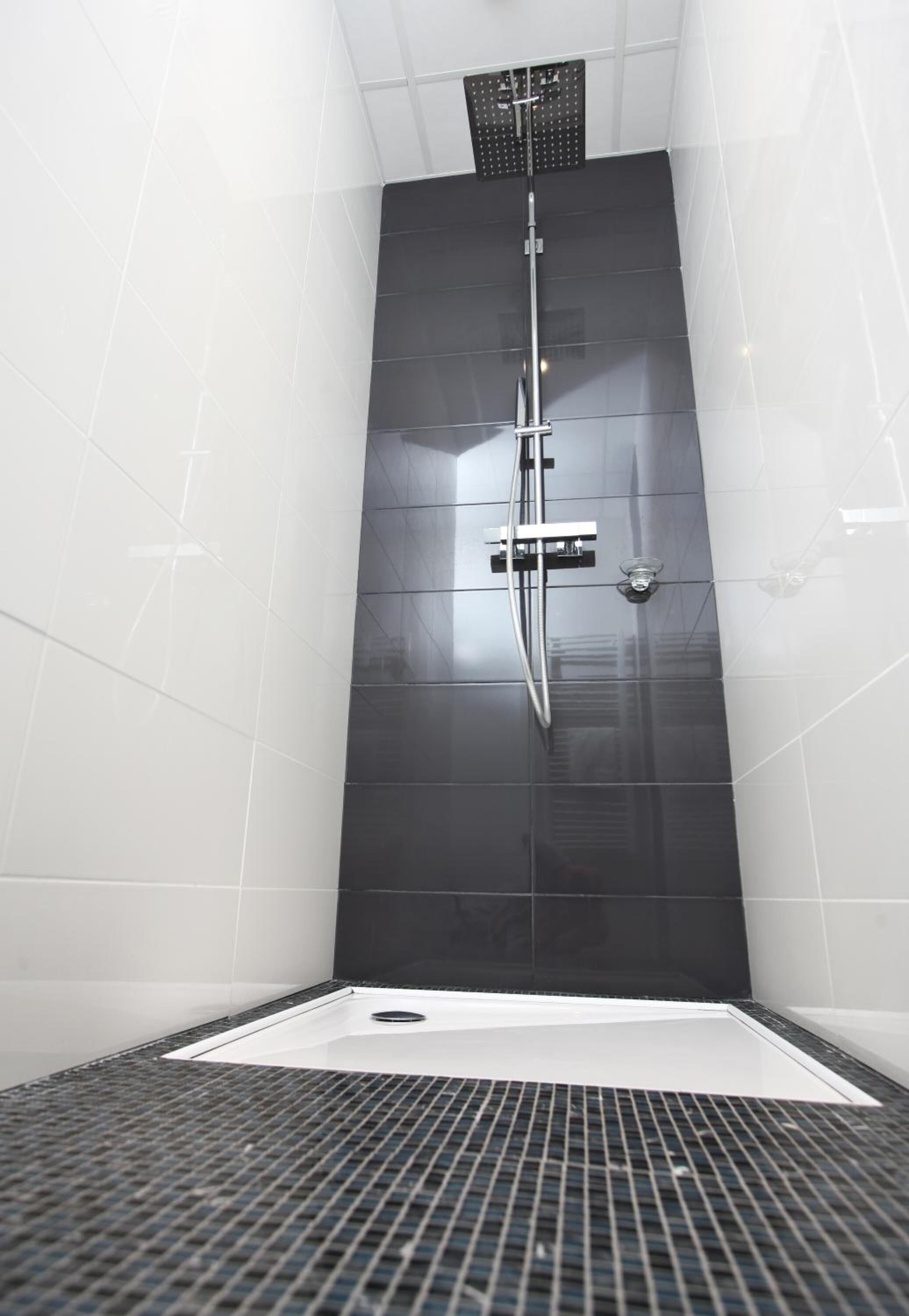 A modern shower with a vertical rain showerhead, a control panel, and a drain in a tiled room.