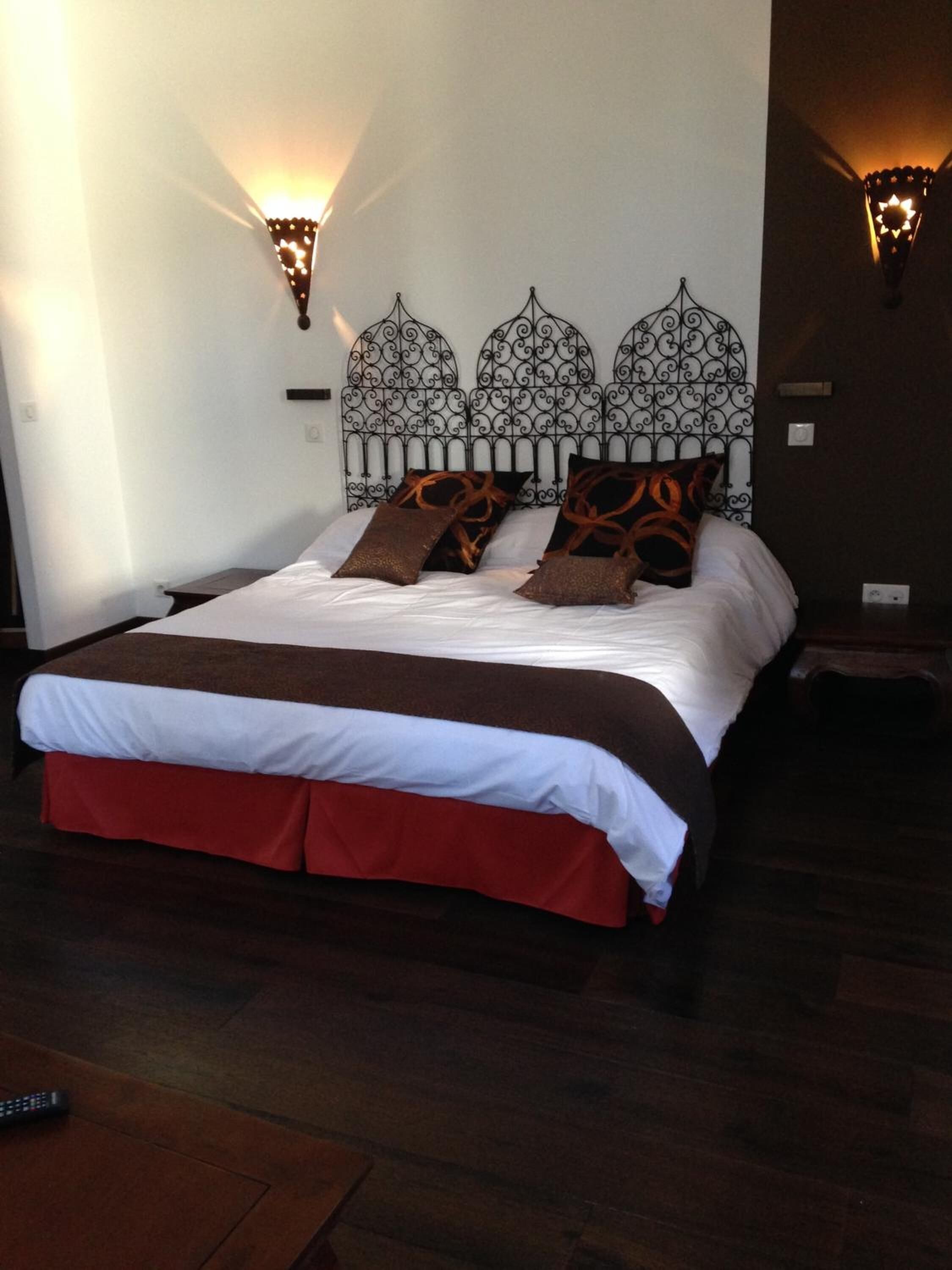 A bed with a metal headboard, two wall sconces, and a remote control on the floor.