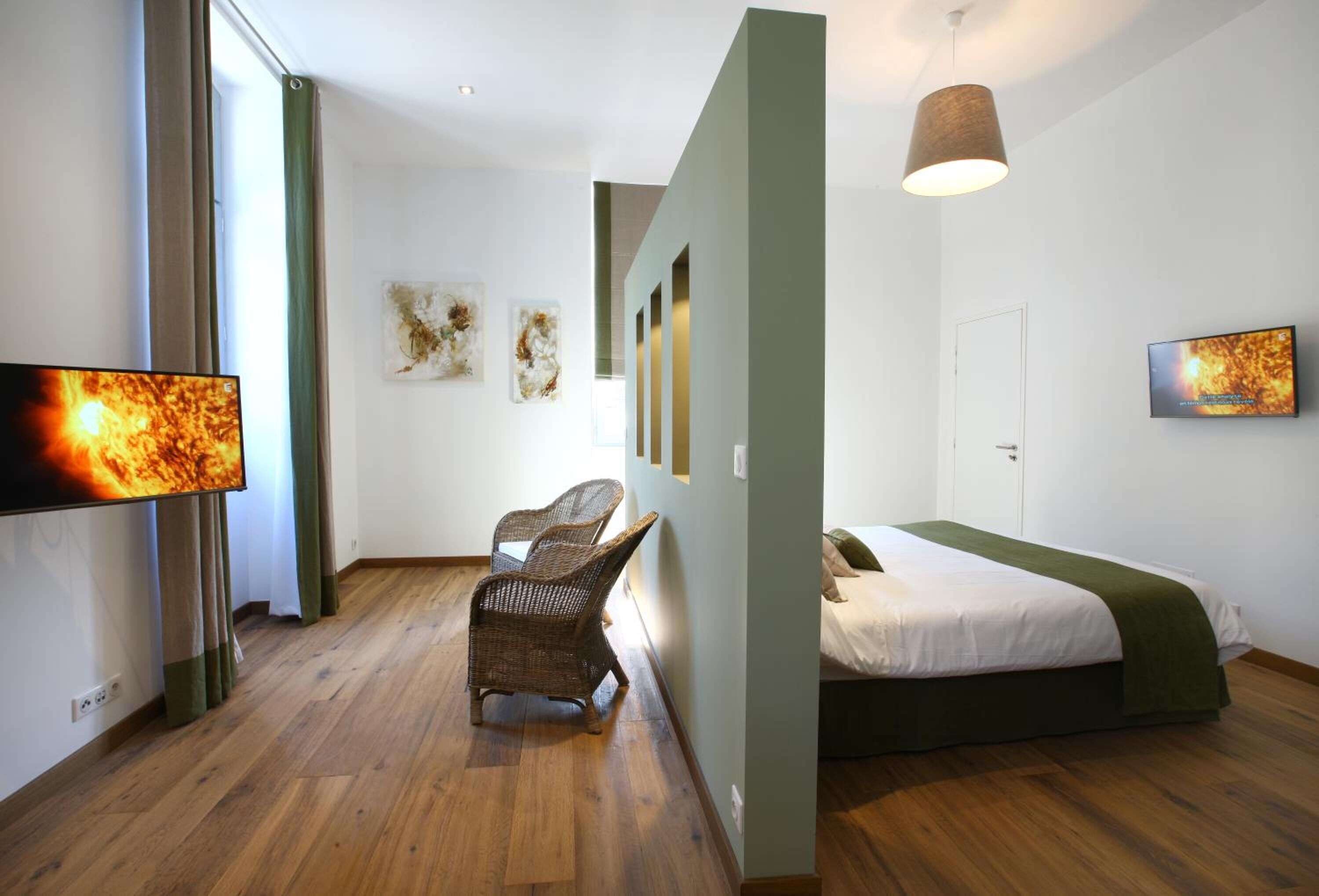 Una habitación de hotel moderna con una cama grande, un escritorio y una silla. Hay obras de arte en las paredes y un televisor a la izquierda.